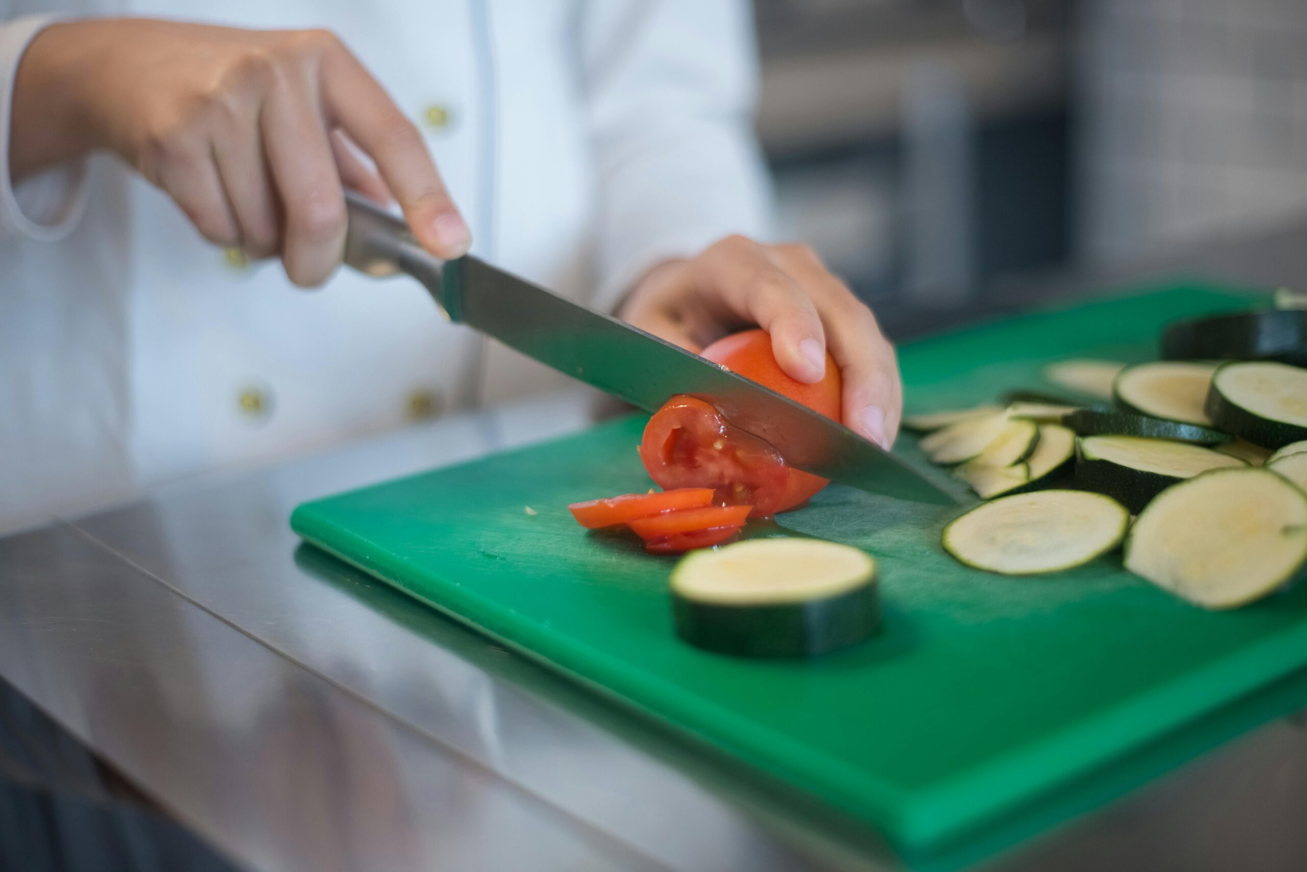 Chef precisely slices tomato and zucchini on green board, enhancing culinary presentation.