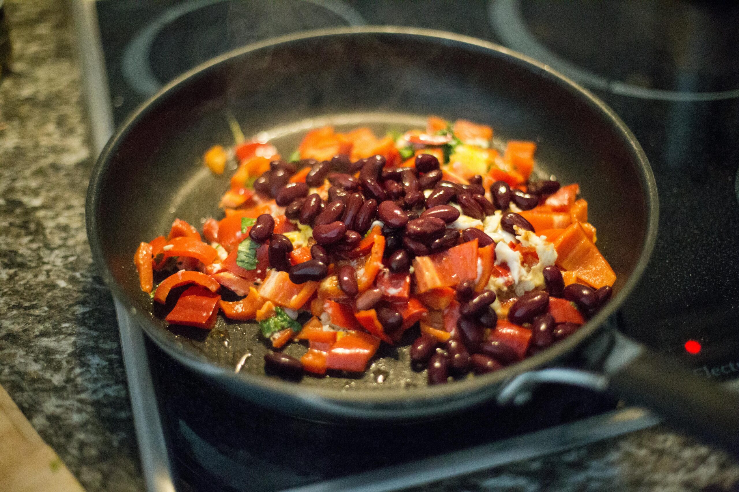 Close-up of bell peppers and beans in a frying pan on a stove, perfect for healthy meal prep.